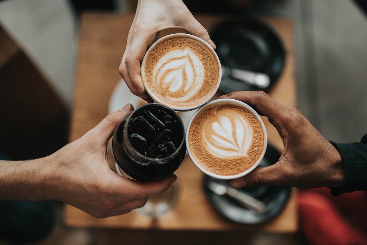 Tres personas brindando con tazas de café en un comercio adherido